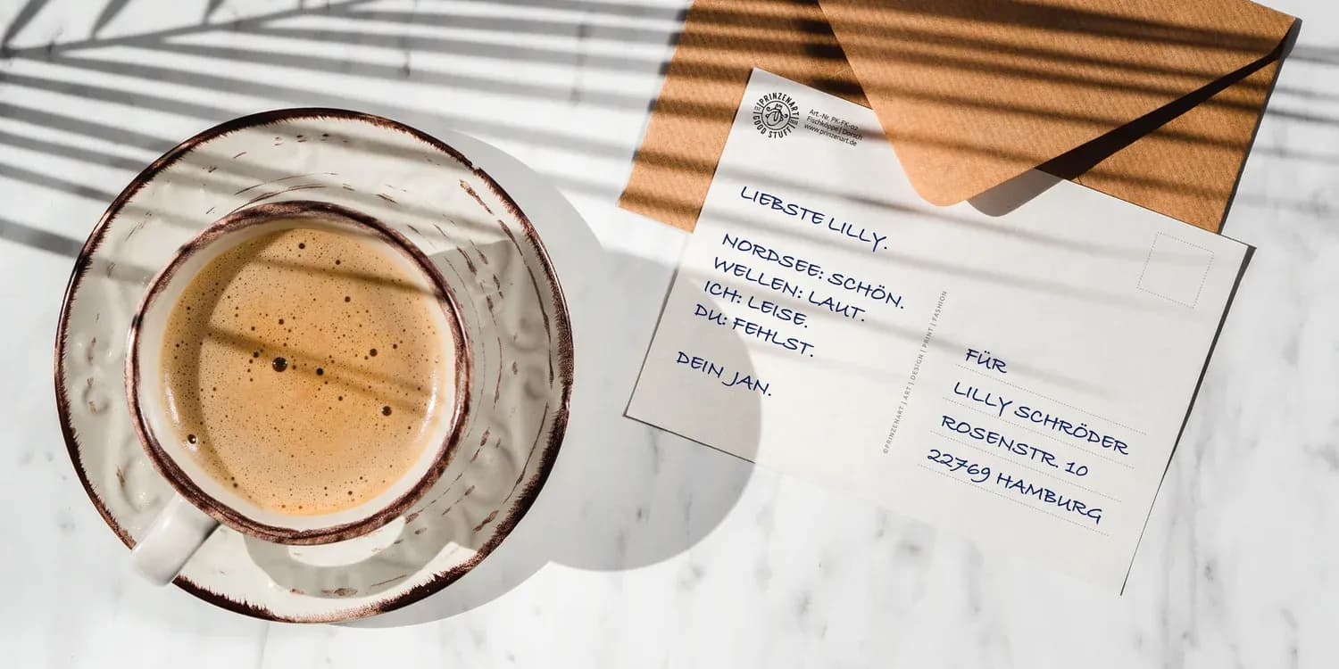 Kaffeetasse und Postkarte auf hellem Tisch, sonnig